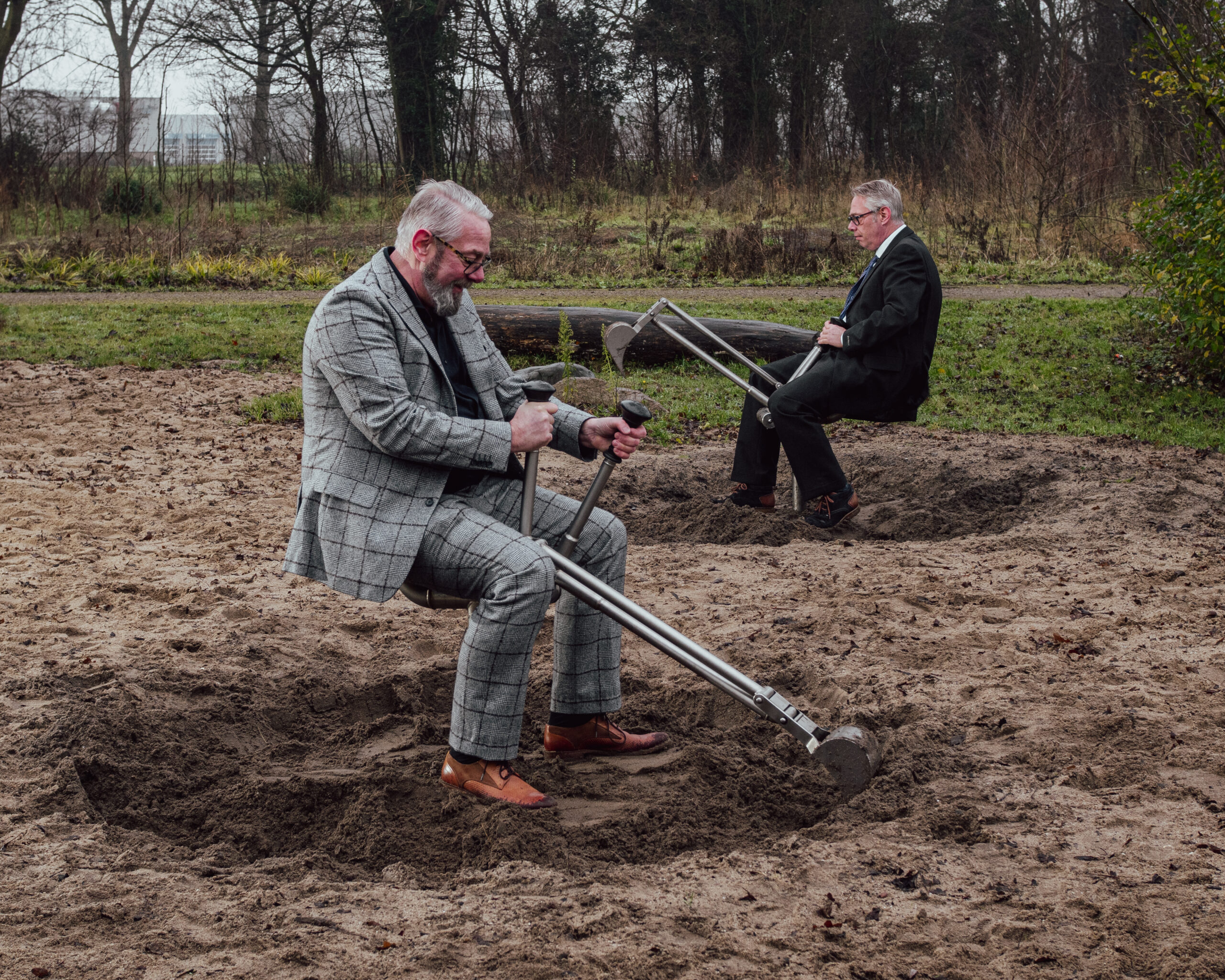 Twee mannen op graafmachines in een speeltuin – speels en symbolisch beeld voor samenwerking, balans tussen werk en plezier, en creatieve aanpak bij Amstellie Studio.