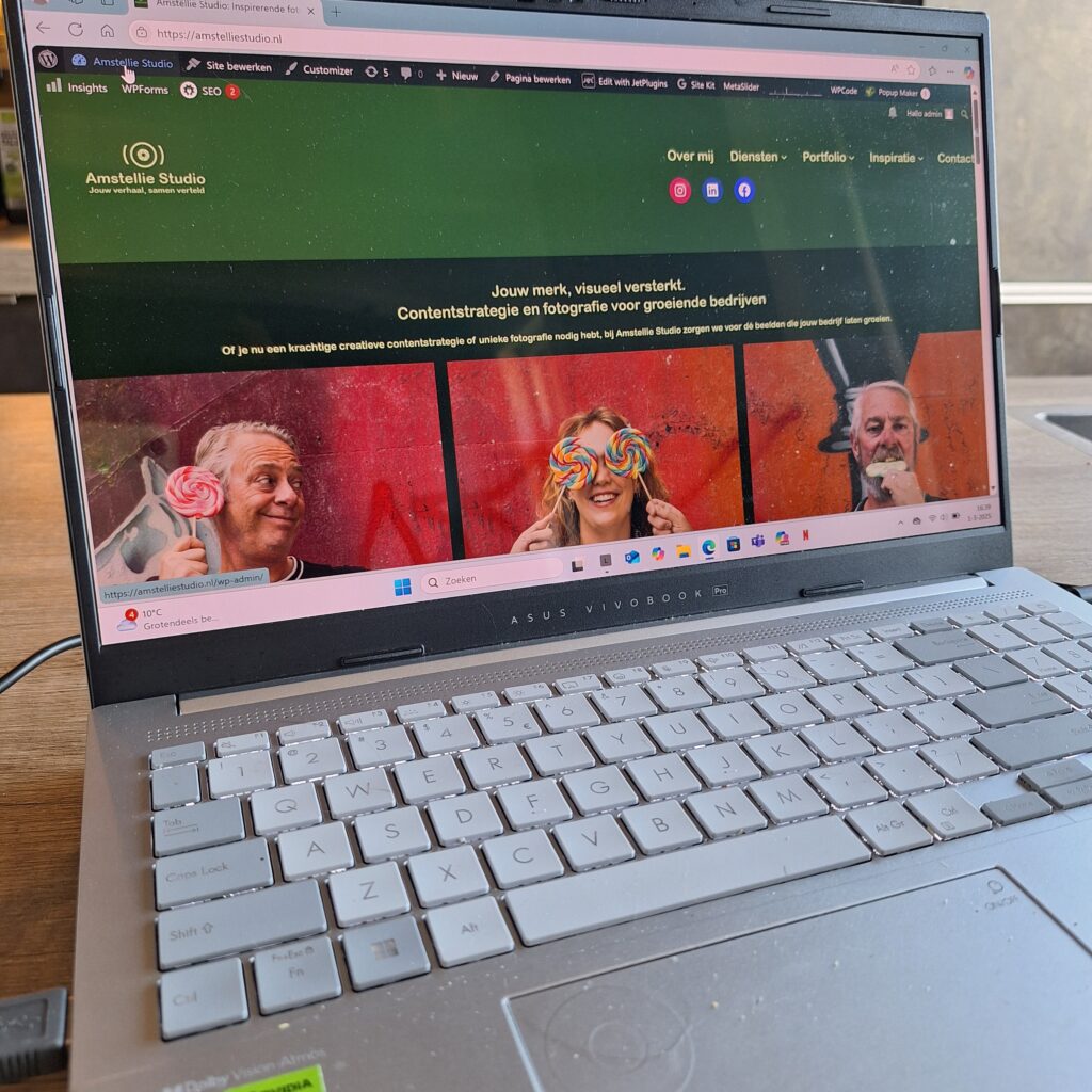 Laptop met typende handen, foto’s en schetsen op tafel – weergave van creatieve tekst- en beeldontwikkeling bij Amstellie Studio.