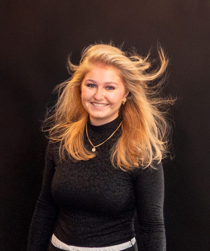 Creatief portret van een vrouwelijke stylist met subtiel glimlachende expressie, stijlvol vastgelegd door Amstellie Studio.